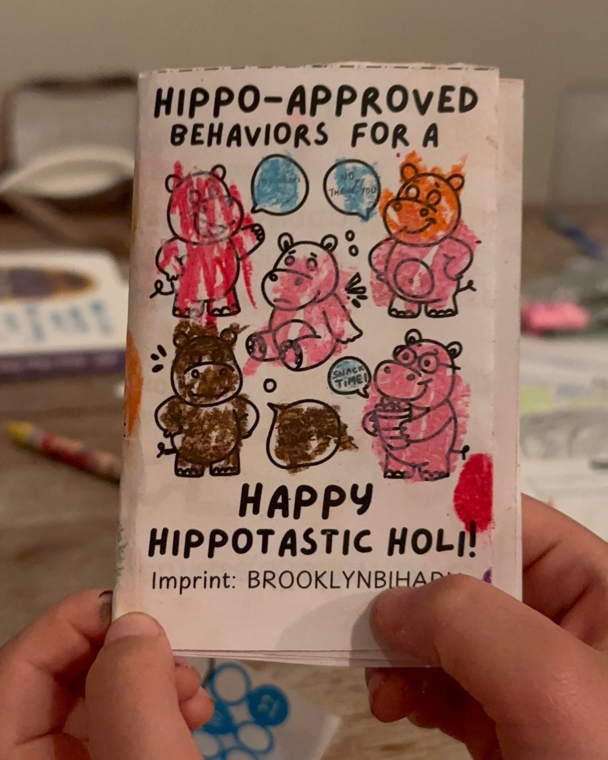 Hippo-Approved Holi mini zine cover, colored in, held by a child