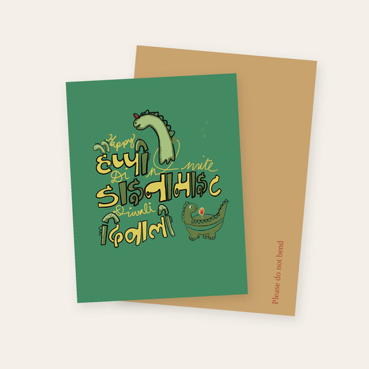 Happy Dinomite Diwali greeting card in green, with dinosaurs and lettering in English and Devanagari, with its kraft mailer.