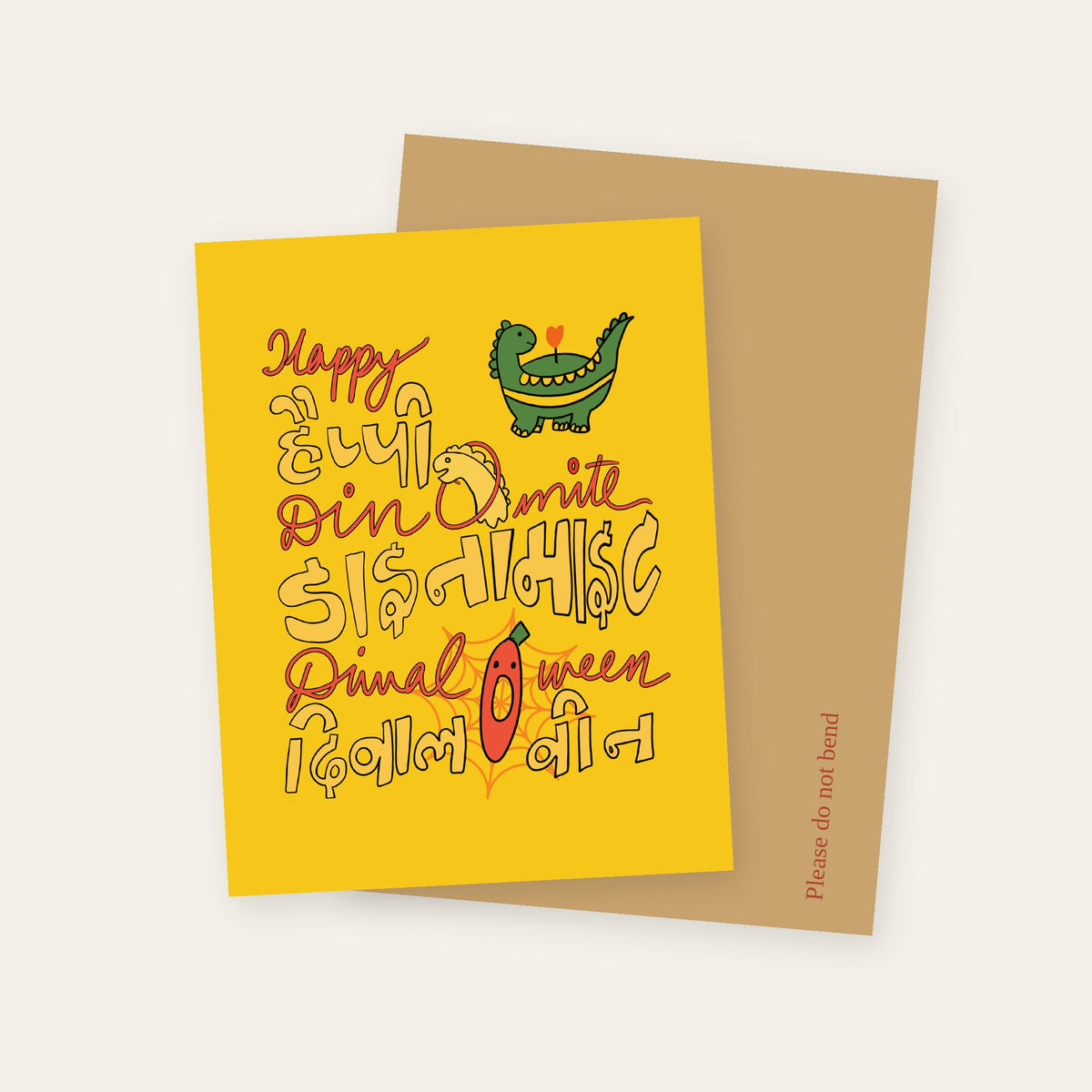 Happy Dinomite Diwal-O-ween greeting card in yellow, with a dinosaur and lettering in English and Devanagari, with its kraft mailer.