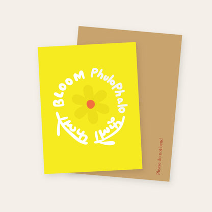 Flower Bloom greeting card in yellow, with Bloom and Phulo Phalo lettered in English and Devanagari around a flower, with its kraft mailer.