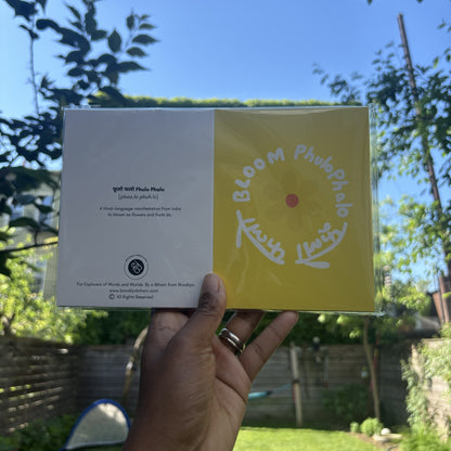Hand holding the Flower Bloom Phulo Phalo greeting card in its clear sleeve, outdoors.