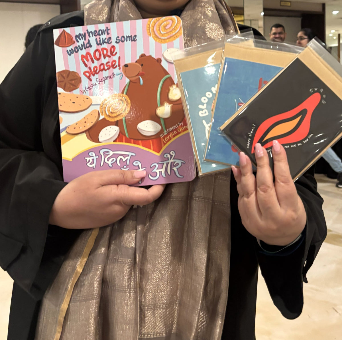 Hands holding Type Storytelling greeting cards and a BROOKLYNBIHARN book at the Chicago Indian Literature Festival.
