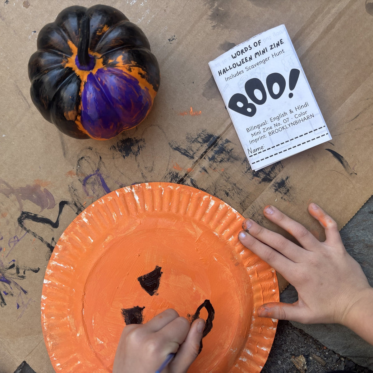 Words of Halloween mini zine on a craft table with a painted pumpkin and paper plate